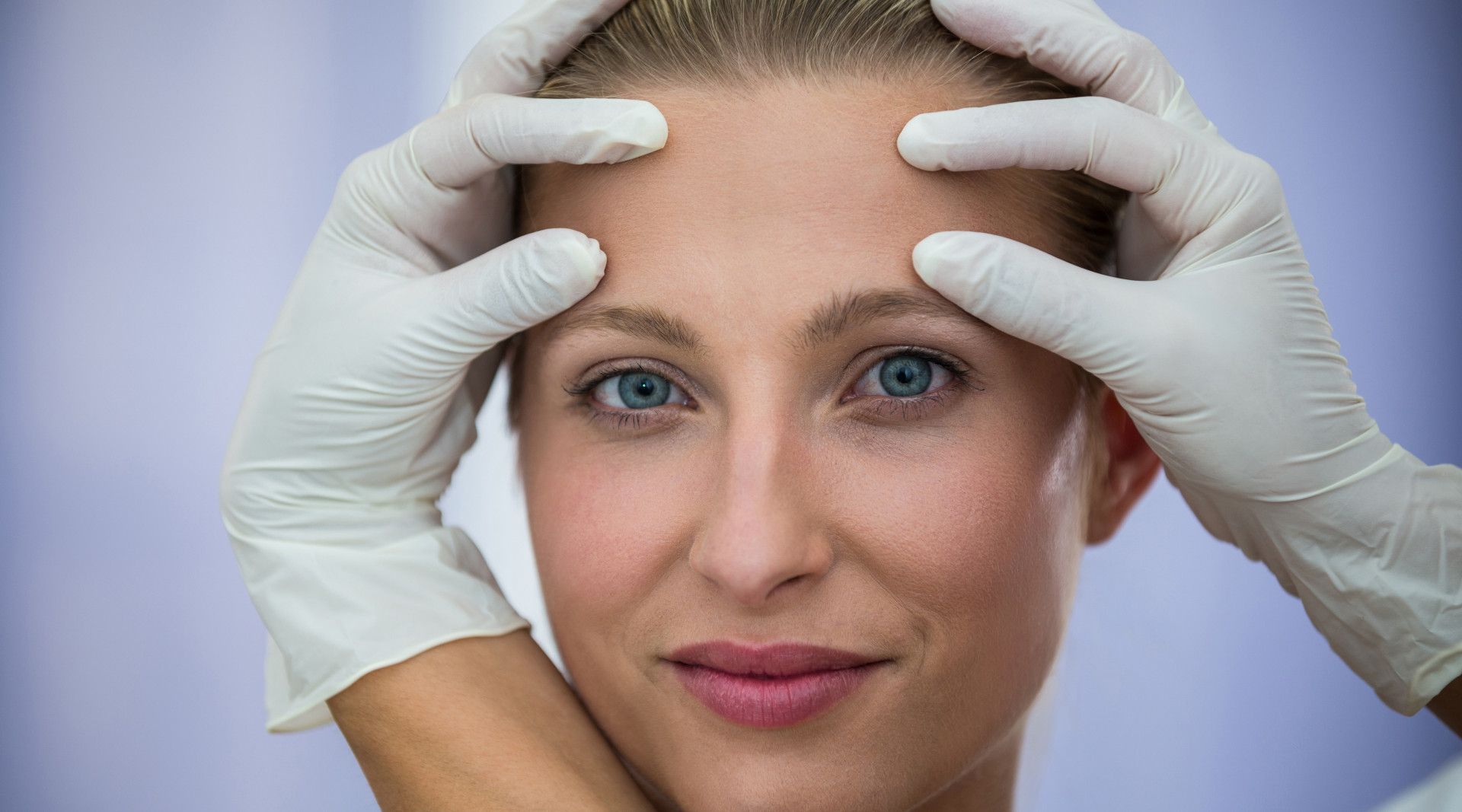 Hände mit medizinischen Handschuhen grenzen Stirnbereich einer Patientin ein