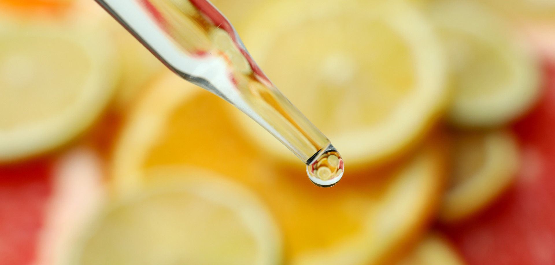 Hintergrund aufgeschnittene Zitrusfrüchte, Vordergrund Pipette mit Tropfen einer Vitaminlösung